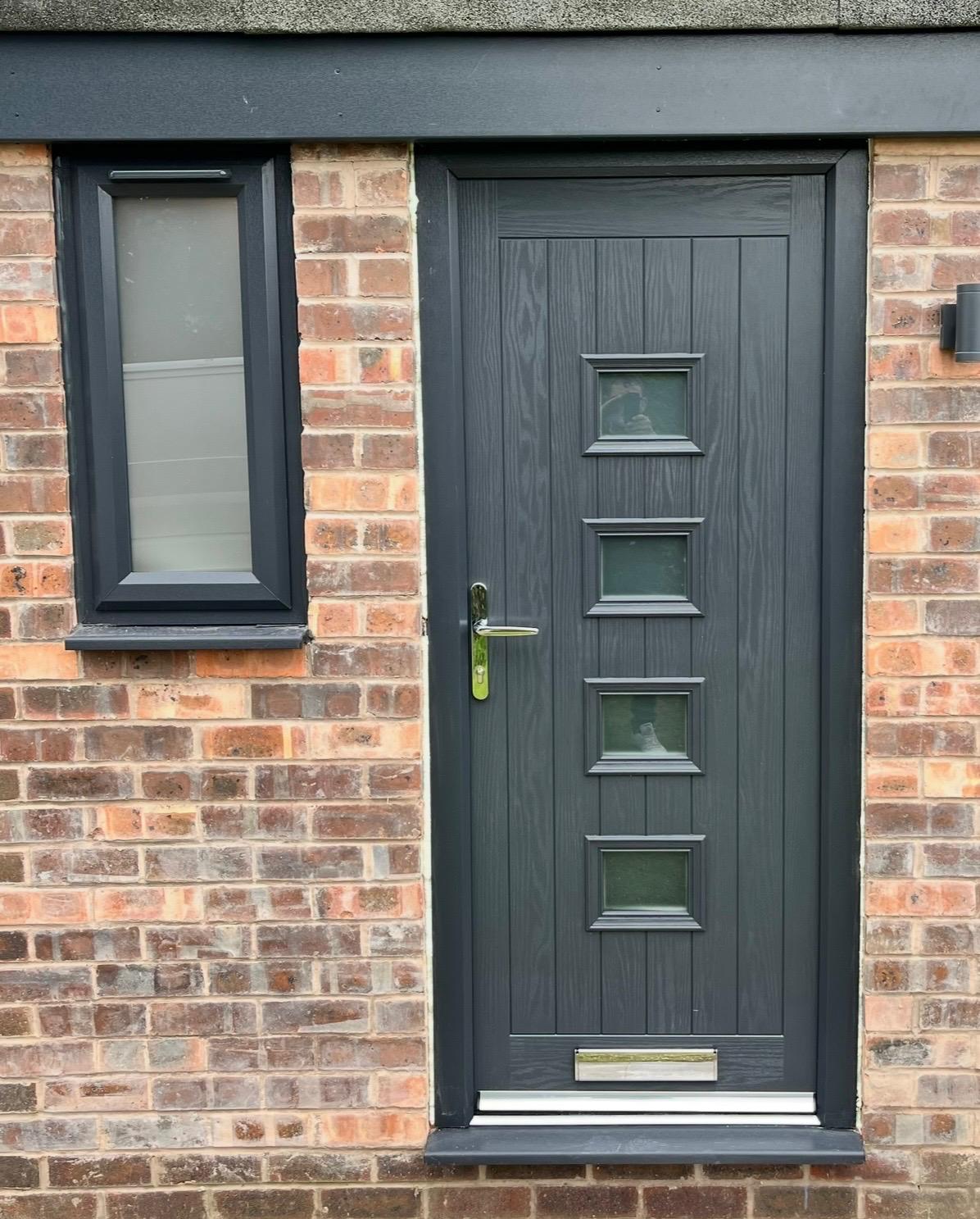 Anthracite grey composite front door with four glazed panels in a brick wall
