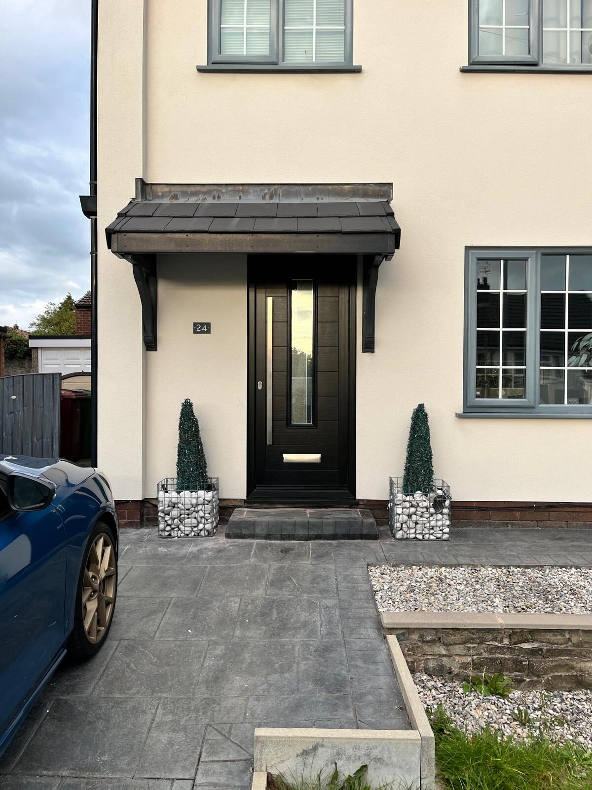 Black composite front door with a glazed panel under a tiled canopy