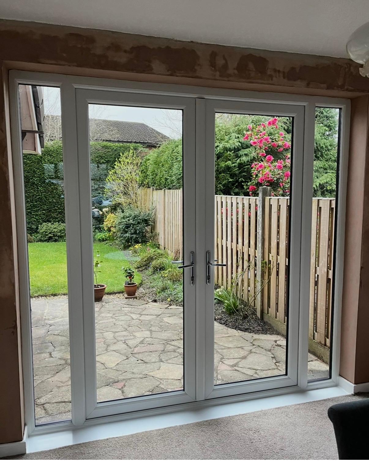 Grey uPVC French doors with glazed side lights opening onto a garden patio