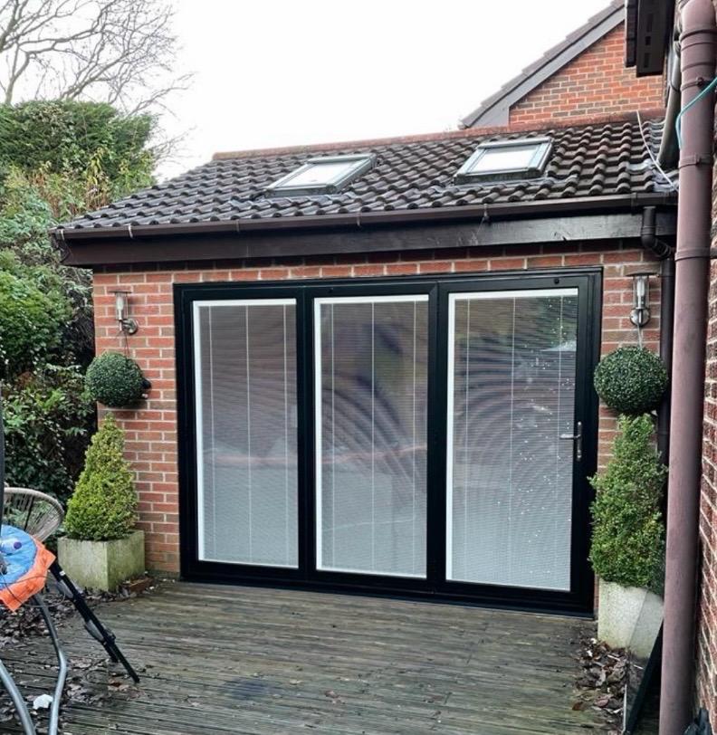 Black bi-folding doors with integral blinds fitted to a brick garden room extension