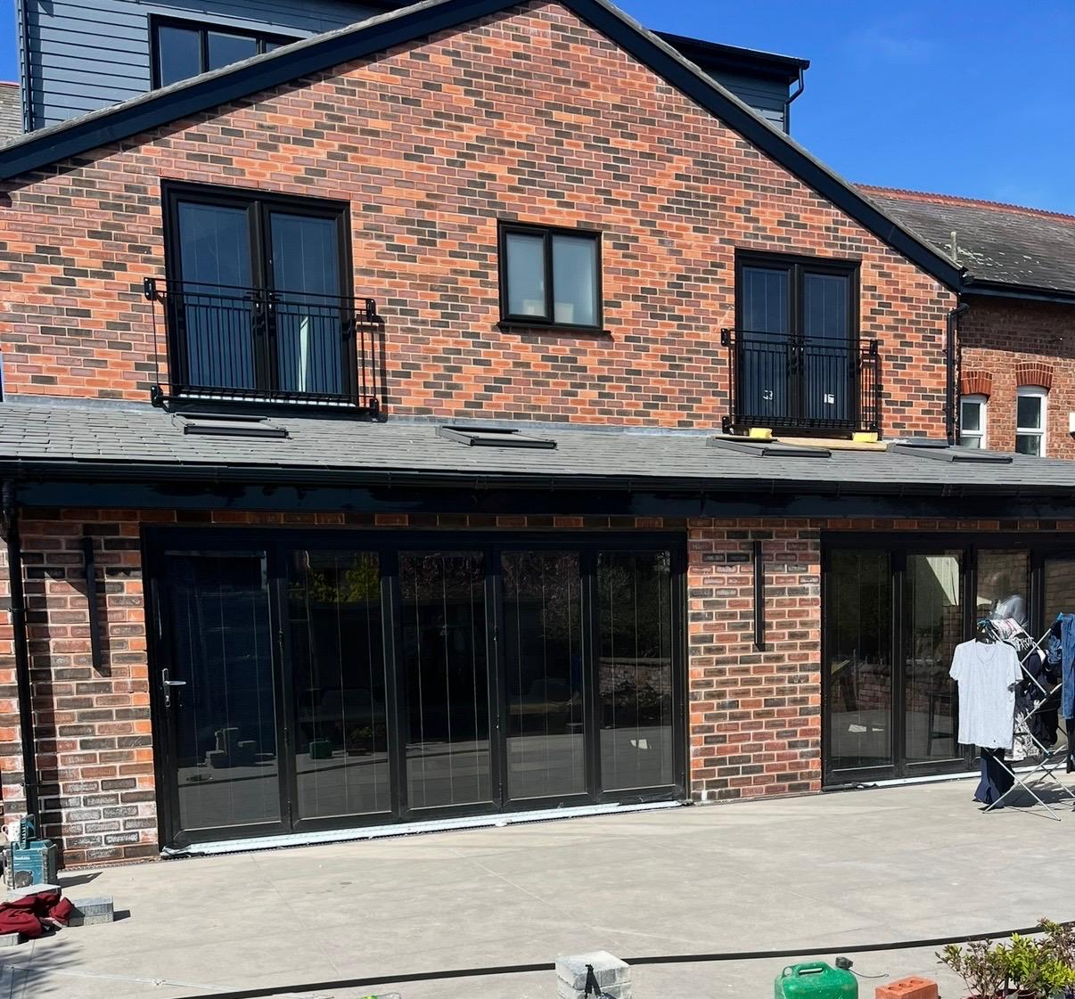 Black bi-folding doors and Juliet balcony windows on a red brick rear extension